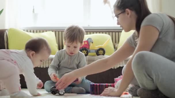 La infancia, la familia, la maternidad, el concepto de paternidad: la joven madre feliz pasa tiempo jugando bloques de imanes construye un castillo con niños pequeños. Alegría Los niños se divierten juntos en el piso de la sala de juegos — Vídeo de stock