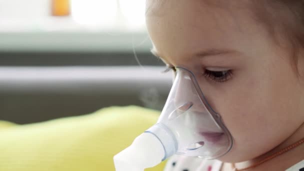 Close-up Kaukasische 3-4 jaar minderjarige kleuter met het masker van een inhalator op een gele grijze bank. Baby die ademhalingstherapie krijgt met vernevelaar. geneeskunde en gezondheid, pediatrie, covid-19 concept — Stockvideo