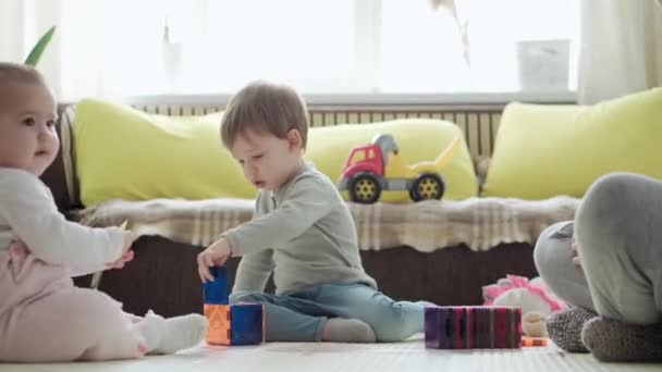Dětství, rodina, mateřství, rodičovství koncept - mladá šťastná matka tráví čas hraním magnetů bloky staví hrad s batole děti. Radost Děti bavte se spolu v herně na podlaze — Stock video