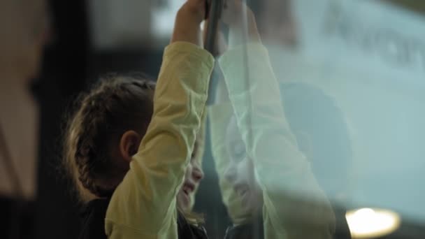 Gros plan de mignonne petite slave caucasienne avec deux épillets enfant d'âge préscolaire mineur dans un café jouant près de la cloison de verre et son reflet. Enfance, cafés et restaurants, concept de jeux — Video