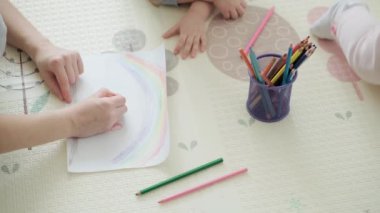 Otantik iki mutlu kardeş yaratıcı çocuklar anneleriyle birlikte kalemle çiziyorlar bahar geliyor resim gökkuşağı içeride, oyun odasında yerde eğleniyor. Çocukluk, Sanat, Eğitim, Yaratıcılık, annelik kavramı