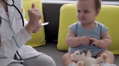 Tıp ve sağlık, pediatri, covid-19 konsepti - Kafkas Slav kökenli genç kadın hemşire ya da doktor çocuk doktorunu 8-12 aylık bebeği sarı gri kanepede muayene ediyor.