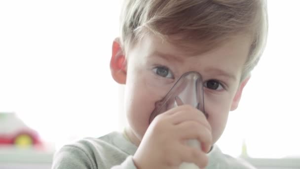 Primer plano Caucásico 3-4 años niño preescolar menor en la máscara de un inhalador en el sofá gris amarillo. Bebé tomando terapia respiratoria con nebulizador. medicina y salud, pediatría, concepto covid-19 — Vídeos de Stock