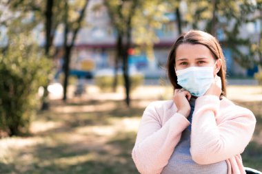 Bakım, bebekler, ilkbahar, koronavirüs ve karantina konsepti - Genç, uzun saçlı, Avrupa Kafkasyalı kadın, öğle vakti güneş ışığında mavi tıbbi koruyucu maske takıldı.