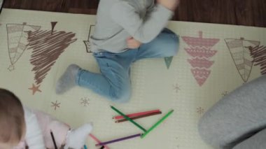 Otantik iki mutlu kardeş yaratıcı çocuklar anneleriyle birlikte kalemle çiziyorlar bahar geliyor resim gökkuşağı içeride, oyun odasında yerde eğleniyor. Çocukluk, Sanat, Eğitim, Yaratıcılık, annelik kavramı