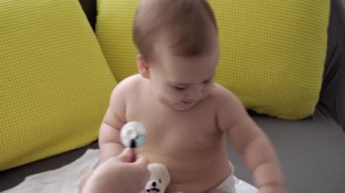 Tıp ve sağlık, pediatri, covid-19 konsepti - Kafkas Slav kökenli genç kadın hemşire ya da doktor çocuk doktorunu 8-12 aylık bebeği sarı gri kanepede muayene ediyor.