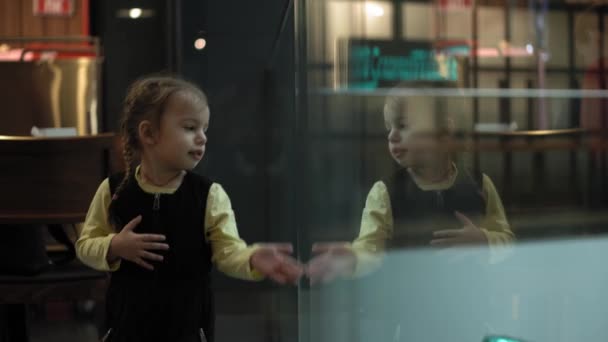 Gros plan de mignonne petite slave caucasienne avec deux épillets enfant d'âge préscolaire mineur dans un café jouant près de la cloison de verre et son reflet. Enfance, cafés et restaurants, concept de jeux — Video