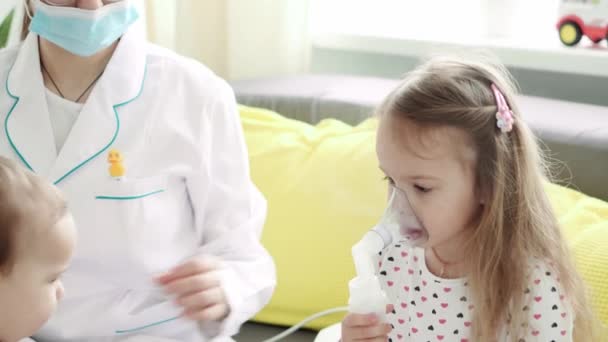 Primer plano de la enfermera joven o pediatra médico hace Procedimiento de inhalación para niños de 3-4 años niña preescolar en el sofá gris amarillo. Lindo bebé en máscara de inhalador. cuidar de un niño enfermo — Vídeos de Stock