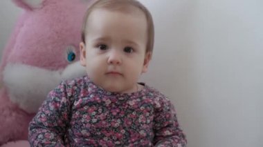 Otantik, küçük, bebek, tombul, renkli elbiseli bir kız çocuğu. Oturuyor ve çocuk odasında beyaz arka planda kafasını sallıyor. Ebeveynlik, çocukluk, yaşam konsepti