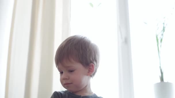 Vertikale Pfanne Nahaufnahme authentisch kranken kleinen Vorschulkind aufgeregt Kind 2-3 Jahre untersucht und liest Buch mit offenem Mund gegenüber Fenster auf gelb-grauem Sofa. Kindheit, Leben, Medizinkonzept — Stockvideo