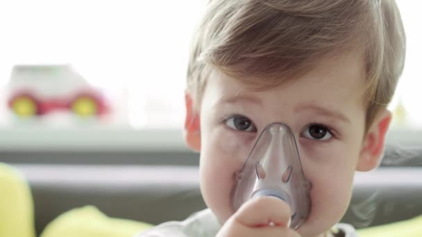 Close-up Kaukasische 3-4 jaar kleine kleuter met het masker van een inhalator op een gele grijze bank. Baby die ademhalingstherapie krijgt met vernevelaar. geneeskunde en gezondheid, pediatrie, covid-19 concept — Stockvideo