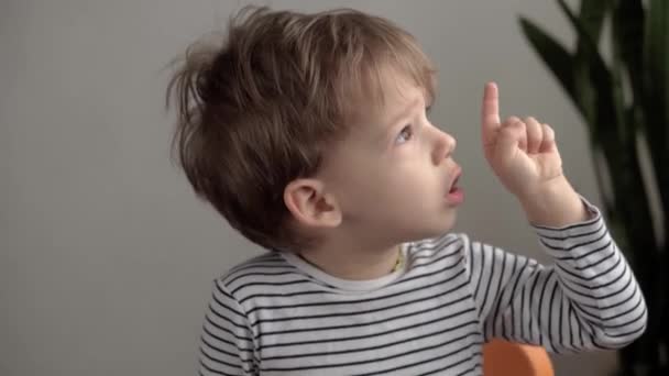 Primer plano auténtico niño preescolar menor mira a la cámara y señala el dedo en los labios y la boca. retrato de niño enfermo con verrugas pequeñas o moluscos en la cara. medicina y salud, concepto de pediatría — Vídeo de stock