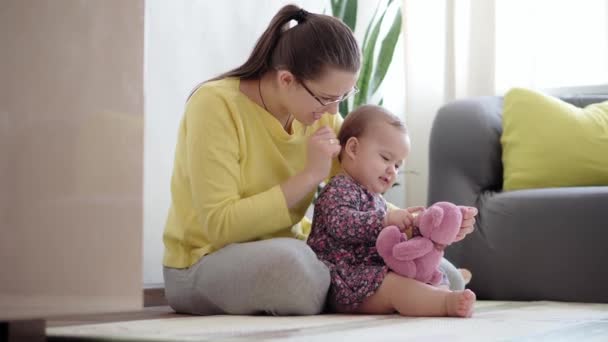 Auténtica toma de cerca de la joven madre neo caucásica que se mantiene en brazos y acaricia al bebé recién nacido en el vivero en el piso de la estera. infante, maternidad, maternidad, paternidad, infancia, vida, autenticidad — Vídeo de stock