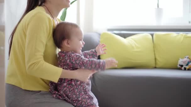 Настоящий крупным планом молодая нео-кавказская мама держит на руках и ласкает ребенка. Младенец учится ходить и падает. новорожденный, материнство, материнство, отцовство, детство, жизнь, понятие подлинности — стоковое видео