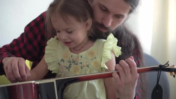 Šťastný muž v rockovém stylu tráví čas s batole dítě hraje na kytaru v útulném domě. otec učit malou dceru hrát na hudební nástroj těšit domácí hudební lekci. rodina, vzdělávání, životní koncept — Stock video