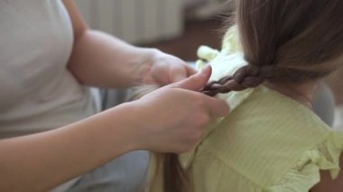 Otantik, genç, beyaz bir kadın annesi, çocuk örgüleriyle ilgileniyor sarı saçlı sarı saçlı kız örgüleri, gri kanepe üzerinde. Örgü örme işlemi. Moda ve güzellik, annelik kavramı.