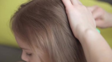 Otantik, genç, beyaz bir kadın annesi, çocuk örgüleriyle ilgileniyor sarı saçlı sarı saçlı kız örgüleri, gri kanepe üzerinde. Örgü örme işlemi. Moda ve güzellik, annelik kavramı.