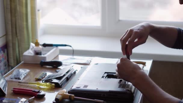 Laptopot javító férfi kezek, csavarhúzóval csavarozott hátsó fedőcsavarok. Elektronikai javítási szolgáltatás. az irodában dolgozó technikus. Telefonjavítás. mérnöki, bontási, fejlett technológiai koncepció — Stock videók