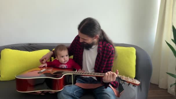 Homme avec barbe noire cheveux longs dans le style rock passer du temps bébé enfant jouer de la guitare à la maison. père enseigner à la petite fille à jouer de l'instrument de musique en profitant de leçons de musique domestique. concept de famille — Video