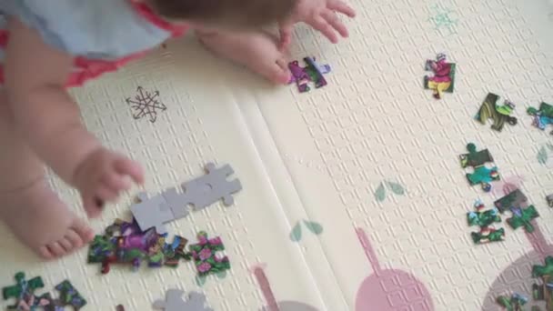 Authentic infant chubby child girl in dress awkwardly barefoot puts jigsaw puzzle top view close up. little baby play alone educational games for motor skills. Childhood, family, insulation concept — Stock Video