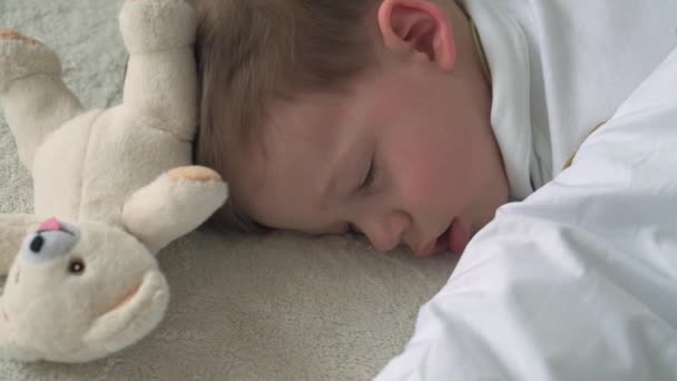 Автентичний крупним планом милий кавказький маленький дошкільний малюк хлопчик 2-3 роки солодко спить у зручному білому ліжку з плюшевим ведмедем. Догляд за дітьми, Спляча дитина, Дитинство, Батьківство, концепція життя — стокове відео
