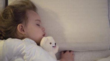 3-4 yıl boyunca tatlı beyaz bir yatakta oyuncak ayıyla tatlı tatlı tatlı uyuyan, beyaz, küçük beyaz bir anaokulu çocuğunun otantik yakın çekimi. Çocuk bakımı, Uyuyan Bebek, Çocukluk, Ebeveynlik, Yaşam Konsepti