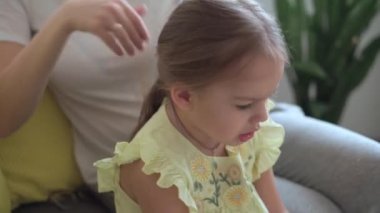 Otantik, genç, beyaz bir kadın annesi, çocuk örgüleriyle ilgileniyor sarı saçlı sarı saçlı kız örgüleri, gri kanepe üzerinde. Örgü örme işlemi. Moda ve güzellik, annelik kavramı.