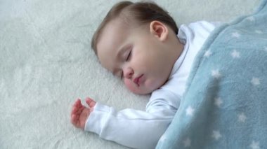 Bebeklik, Rahatlama, Tatlı Rüyalar, Çocukluk, Aile Konsepti - 9-12 aylık küçük bebek kızın Athentic gergin yüzü Öğle Yemeği Uyku modunda battaniyeyle kaplı beyaz yatakta uyur.