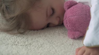 Anaokulunun şirin bebek şakalarının özgün yakın çekimi. Çocuklar ve kızlar oyuncak ayıyla rahat beyaz yatakta tatlı tatlı uyurlar. Çocuk bakımı, Uyuyan Bebek, Çocukluk, Ebeveynlik, Yaşam Konsepti.