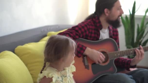 Szczęśliwy człowiek w stylu rocka spędzić czas z maluch dziecko gra na gitarze w przytulnym domu. ojciec śpiewać piosenki dla małej uroczej córki instrument muzyczny cieszyć się lekcji muzyki krajowej. rodzina, miłość, koncepcja życia — Wideo stockowe