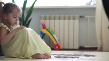 Otantik şirin çocuk anaokulu kızı yere yapboz koyuyor. Küçük çocuk, sarı gri kanepenin yanında motor becerileri için eğitici oyunlar oynuyor. Çocukluk, aile, yalıtım konsepti.