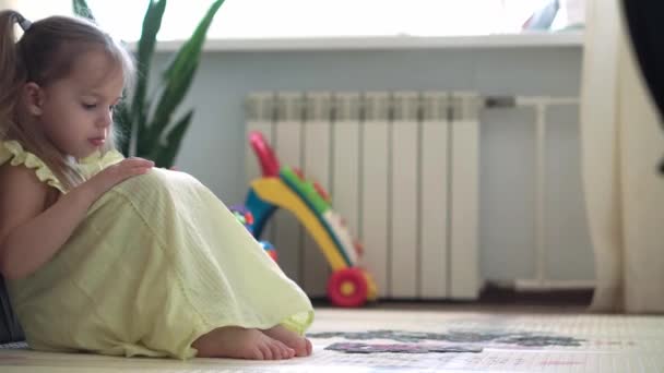 Autentický roztomilý šťastný dítě školka dívka klade puzzle na podlaze zblízka. malý kluk hrát sám vzdělávací hry pro motorické dovednosti v blízkosti žluté šedé pohovky. Dětství, rodina, koncepce izolace. — Stock video
