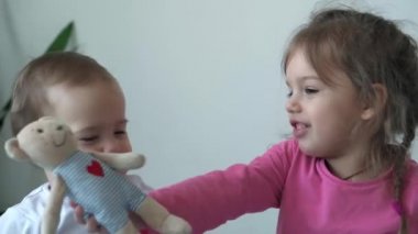 Gerçek iki mutlu çocuk, bebek bebek ve 3-4 yaşındaki kız mavi ve beyaz yatakta yan yana oturuyorlar. Kız kardeşler evdeki kanepede oynuyorlar. Çocukluk, çocukluk, aile, uyku, dinlenme konsepti