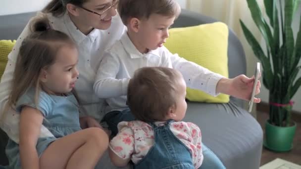 Kaukaski rodzina małe dzieci dziewczynka chłopiec i mama rozmawia w wideokonferencji przez smartfona razem w salonie w domu z uśmiechem szczęścia. aktywność technologia styl życia telefon komórkowy korzystanie koncepcja — Wideo stockowe