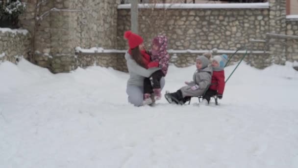 Wakacje, gra, koncepcja rodziny - slo-mo autentyczne trzy szczęśliwe przedszkolne rodzeństwo dzieci z młodą wonan mama sanki i zabawy ze śniegiem. opady śniegu w okresie zimowym w zimowym stoczni na zewnątrz — Wideo stockowe