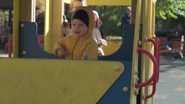 Lapsuus, perhe, äitiys, konsepti Kaksi esikouluikäistä alaikäistä lasta poika ja tyttö 2-4 vuotta veli ja sisko leikkivät äidin kanssa leikkikentällä syksyllä puistossa. pienet lapset hauskaa istua lelu puinen bussi. — kuvapankkivideo