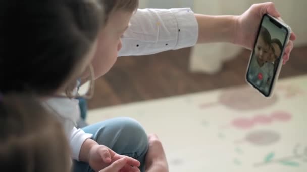 Kaukasische Familie kleine Kinder Mädchen Junge und Mutter sprechen in Videokonferenz per Smartphone zusammen im Wohnzimmer zu Hause mit glücklichem Lächeln. Aktivitätstechnologie Lifestyle Mobiltelefon Nutzungskonzept — Stockvideo