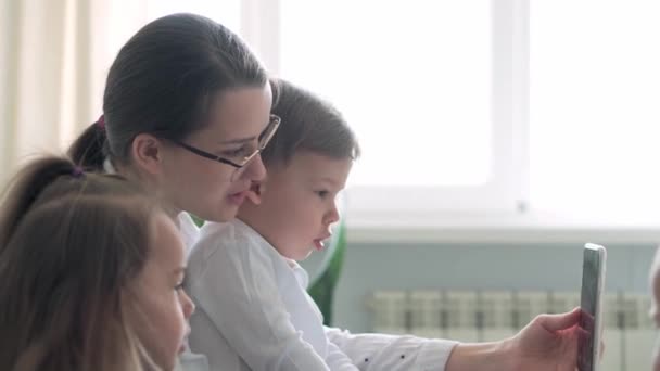 Kaukaski rodzina małe dzieci dziewczynka chłopiec i mama rozmawia w wideokonferencji przez smartfona razem w salonie w domu z uśmiechem szczęścia. aktywność technologia styl życia telefon komórkowy korzystanie koncepcja — Wideo stockowe