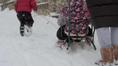 Tatil, oyun, aile kavramı, yavaş çekim otantik üç mutlu anaokulu çocuğu, genç Wonan annesi kızakla kayan ve karla oynayan kardeşleri. Soğuk mevsimde kar yağışı açık havada kış bahçesinde