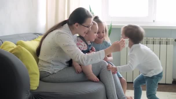 Kaukaski rodzina małe dzieci dziewczynka chłopiec i mama rozmawia w wideokonferencji przez smartfona razem w salonie w domu z uśmiechem szczęścia. aktywność technologia styl życia telefon komórkowy korzystanie koncepcja — Wideo stockowe