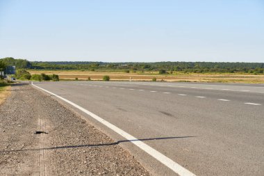 Yumuşak odaklı asfalt yol yüzeyinde, düşük açılı beyaz işaretler var. Yazın ormanlık alan ve yol maviye boyandı. Yüksek kalite fotoğraf. Seyahat, tehnoloji, doğa kavramı.