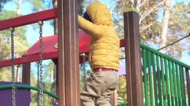 Çocukluk, aile, annelik, etkinlik konsepti - okul öncesi okul 2-4 yıllık turuncu ceketli çocuk Soğuk sonbahar parkında oyun parkında oynuyor. Küçük çocuk köprüde dışarıda iyi eğlenceler.