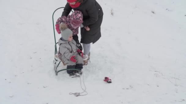 Wakacje, gra, koncepcja rodziny - slo-mo autentyczne trzy szczęśliwe przedszkolne rodzeństwo dzieci z młodą wonan mama sanki i zabawy ze śniegiem. opady śniegu w okresie zimowym w zimowym stoczni na zewnątrz — Wideo stockowe