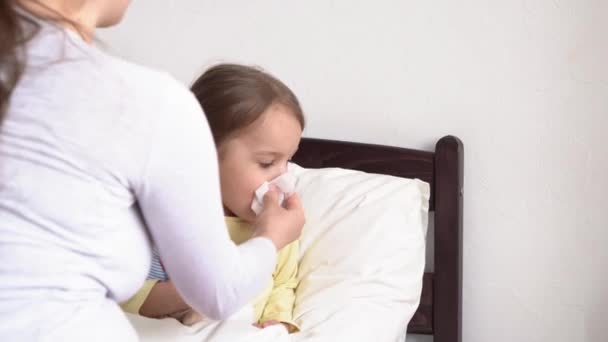 Junge kaukasische Krankenschwester oder Arzt Kinderarzt untersucht Baby Mädchen hilft, pustet Ihre Nase in Serviette auf weißem Bett. Mama kümmert sich um krankes Kind. Medizin und Gesundheit, Mutterschaft, Covid-19-Konzept — Stockvideo