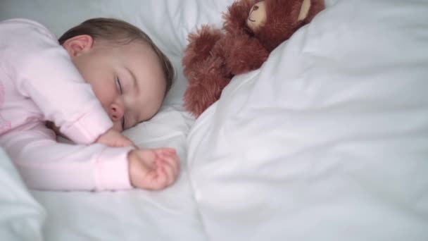 Auténtico retrato lindo bebé caucásico regordete niña o niño en sueño rosa con oso de peluche en la cama blanca. niño descansando a la hora del almuerzo. cuidado, Niñez durmiente, Infancia, paternidad, concepto de vida — Vídeo de stock