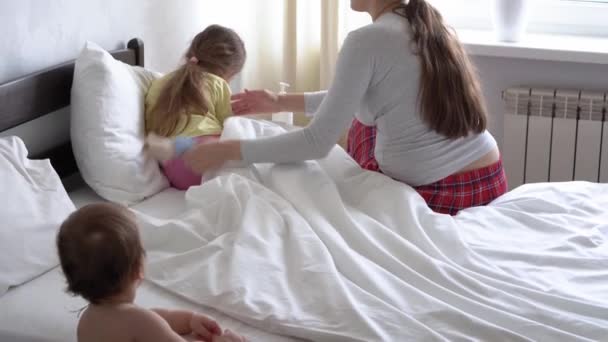 Nahaufnahme authentische junge kaukasische Krankenschwester oder Arzt Kinderarzt untersucht Baby Mädchen geben Teddybär auf weißem Bett. Mama kümmert sich um krankes Kind. Medizin und Gesundheit, Mutterschaft, Covid-19-Konzept — Stockvideo