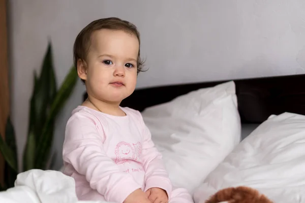 Äkta porträtt kaukasiskt litet spädbarn knubbig liten flicka eller pojke i rosa sömnig när du vaknar tittar på kameran ler söta och grimaser i vit säng. Barnomsorg, Barndom, Föräldraskap, Livskoncept — Stockfoto