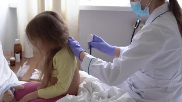 Authentic cute caucasian cute young woman nurse or doctor pediatrician examine with statoscope minor preschool baby girl kid on white bed in hospital. medicine and health, pediatrics, covid-19 concept — Stock Video