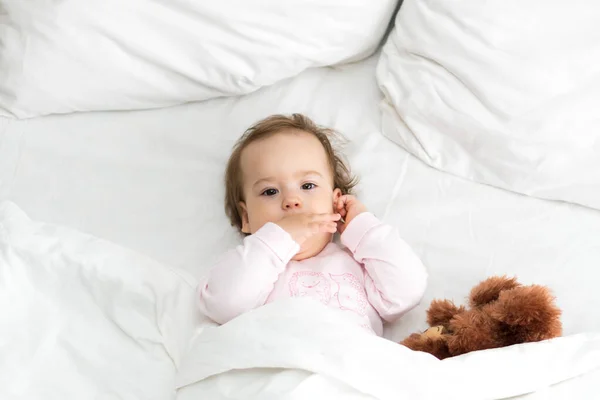 Hiteles portré aranyos kaukázusi kis csecsemő pufók kislány vagy fiú rózsaszín álmos ébredés után maci nézi kamera fehér ágyban. Gyermekgondozás, Gyermekkor, Szülőkor, életmód koncepció — Stock Fotó