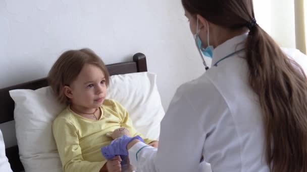 Autentico carino caucasico cute giovane donna infermiera o medico pediatra esaminare con statoscopio minore bambino bambina in età prescolare sul letto bianco in ospedale. medicina e salute, pediatria, concetto covid-19 — Video Stock